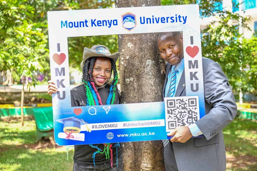 Mount Kenya University graduates celebrating outdoors with a photo frame.
