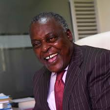 A smiling elderly man in a suit at a desk, professional setting.