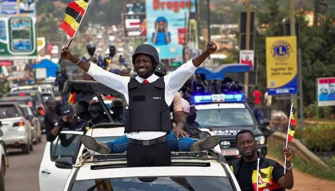 Kenyan man celebrating election victory from vehicle, waving flags, with supporters on busy street.