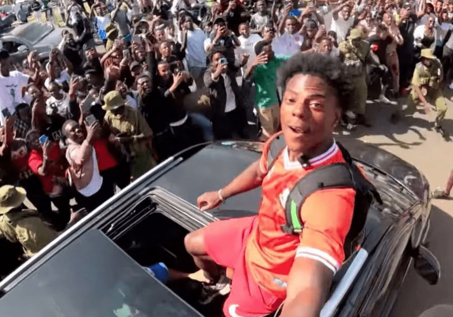 Young man taking selfie from car roof during lively Nairobi street celebration.
