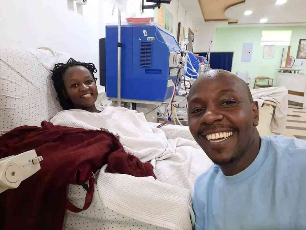 Woman in hospital bed with dialysis machine, smiling, medical treatment.