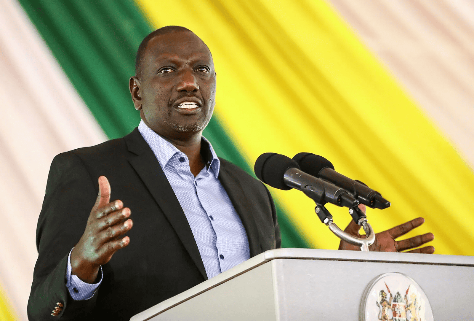 Kenyan politician delivering a speech at a public event, with the national flag in the background.