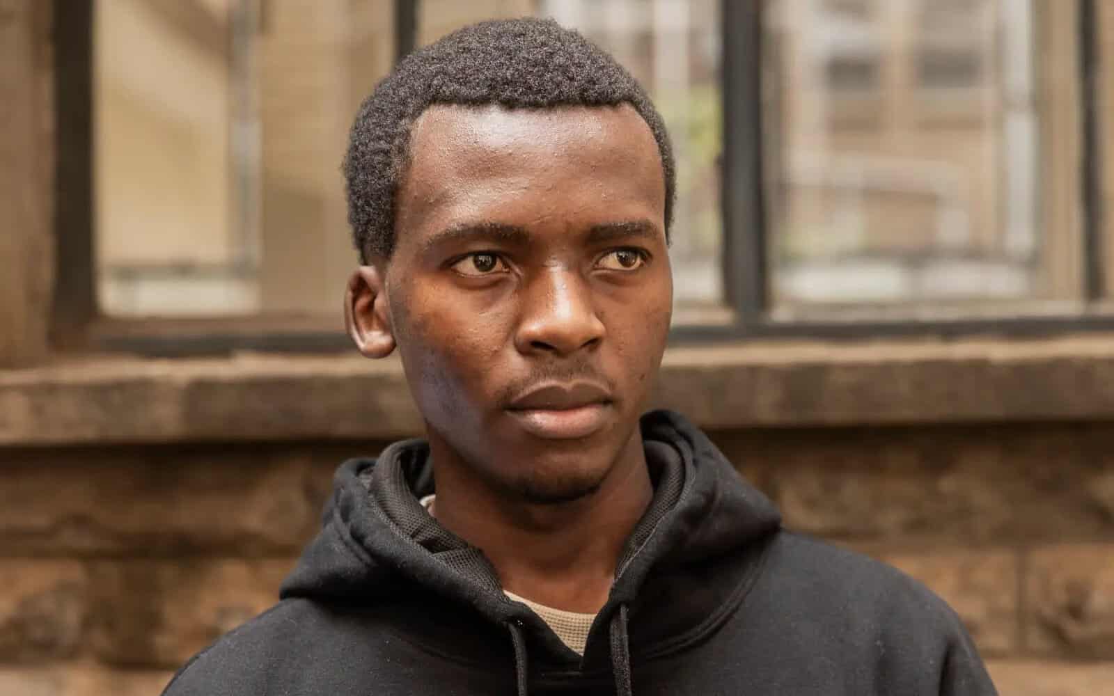 Young man with serious expression outdoors, wearing a black hoodie.