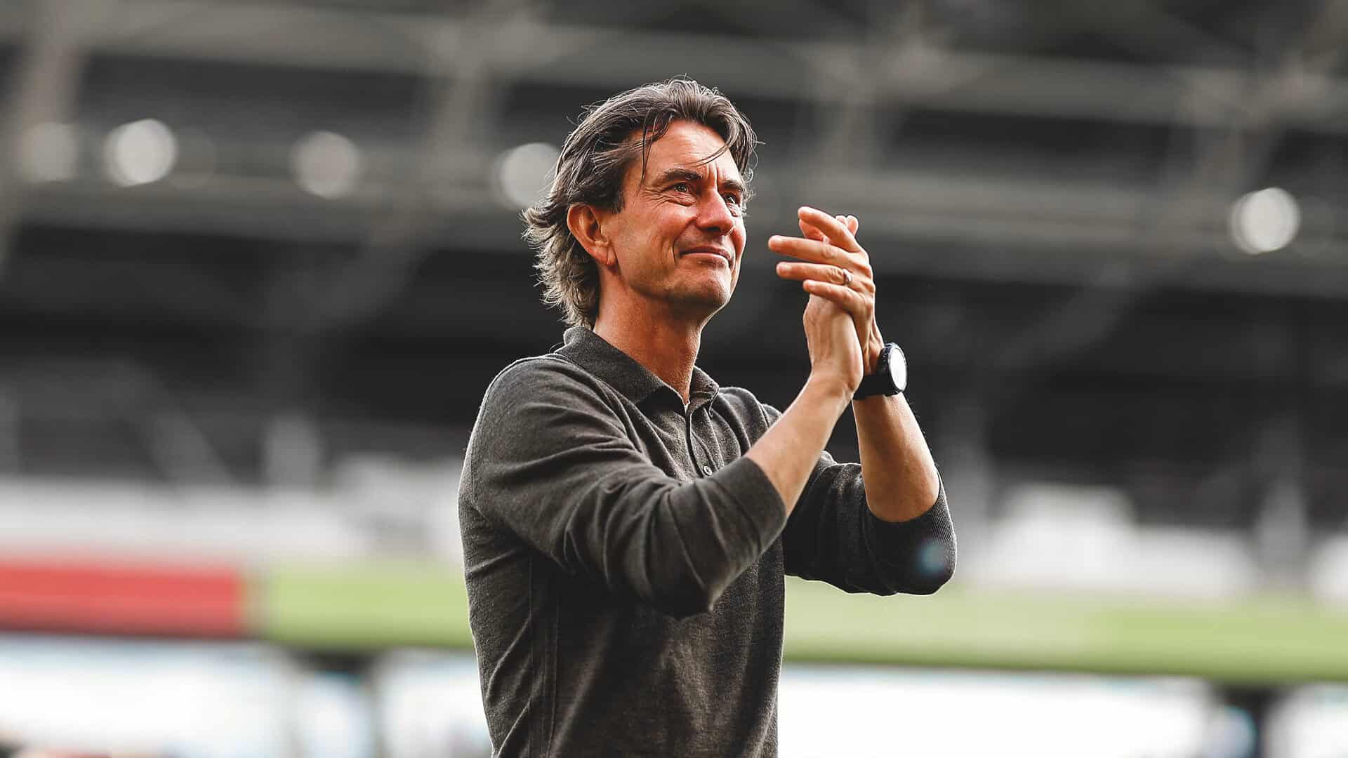 Man applauding at a sports event, celebrating achievement, in a stadium setting.