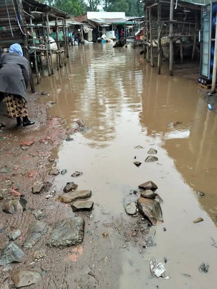 Flooded market street with muddy water and scattered rocks in Kenya.
