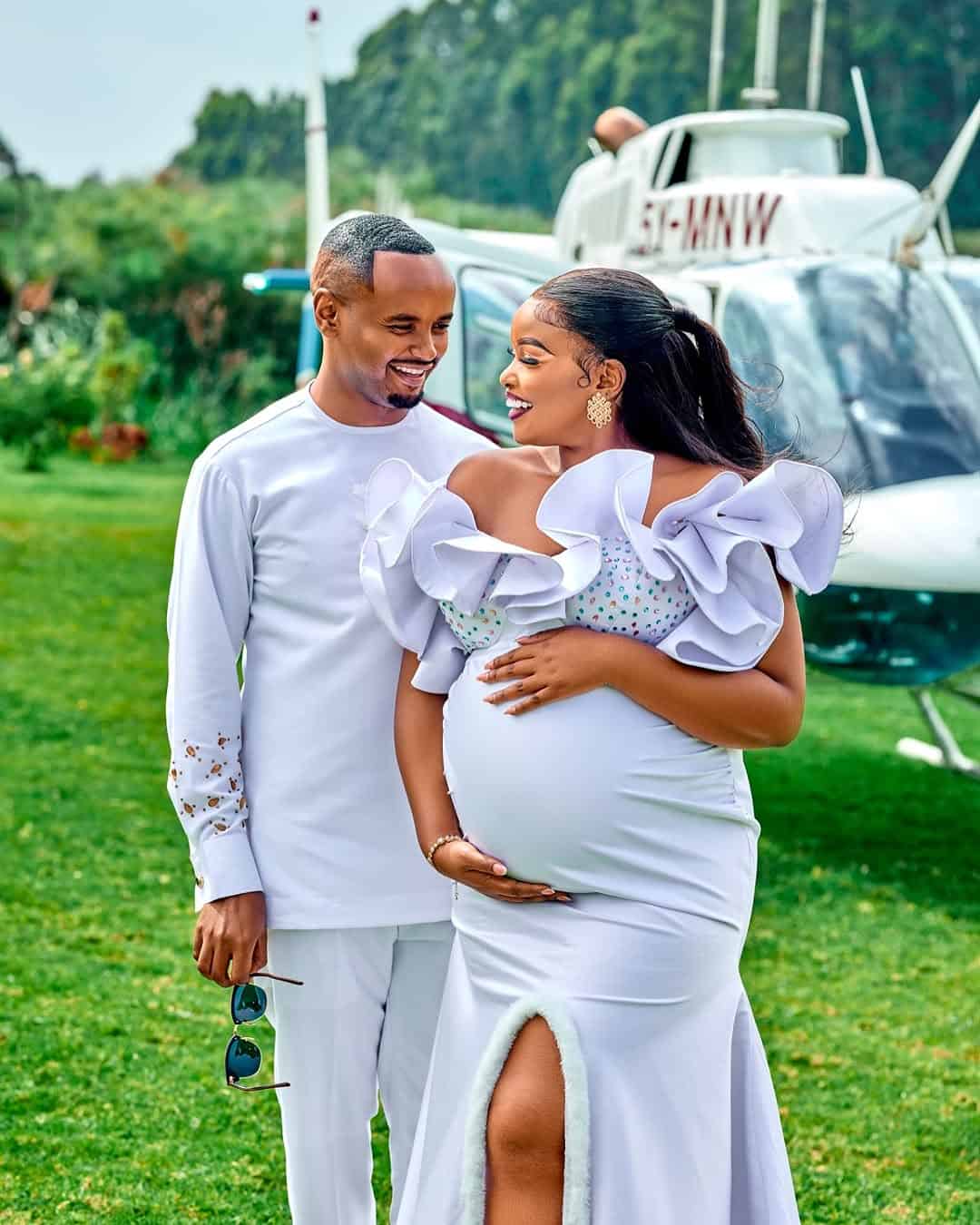 Pregnant woman and partner smiling outdoors near helicopter, celebrating pregnancy.