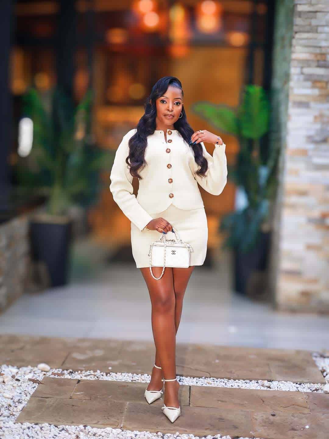 Elegant woman in white outfit posing at KWETU NEWS event in a modern setting.