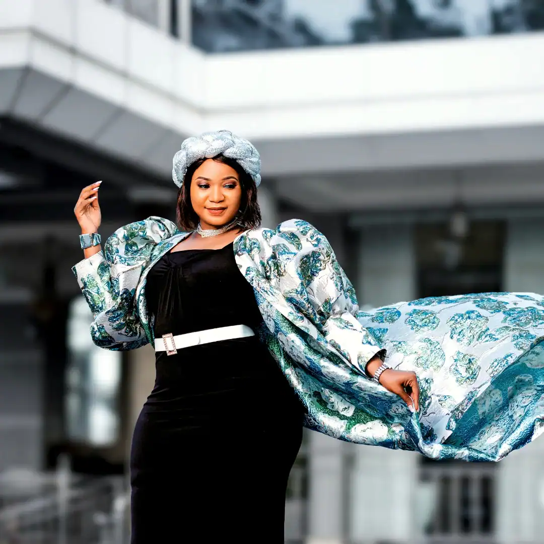 Woman in fashionable outfit with flowing jacket outside modern building, KWETU NEWS.