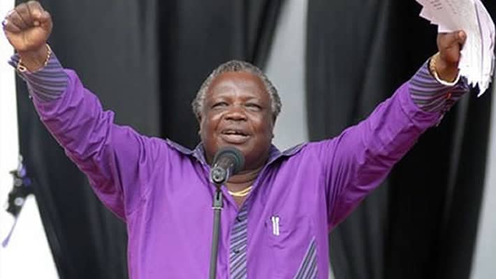 Elderly man speaking passionately at a community event, raising his hands in celebration.