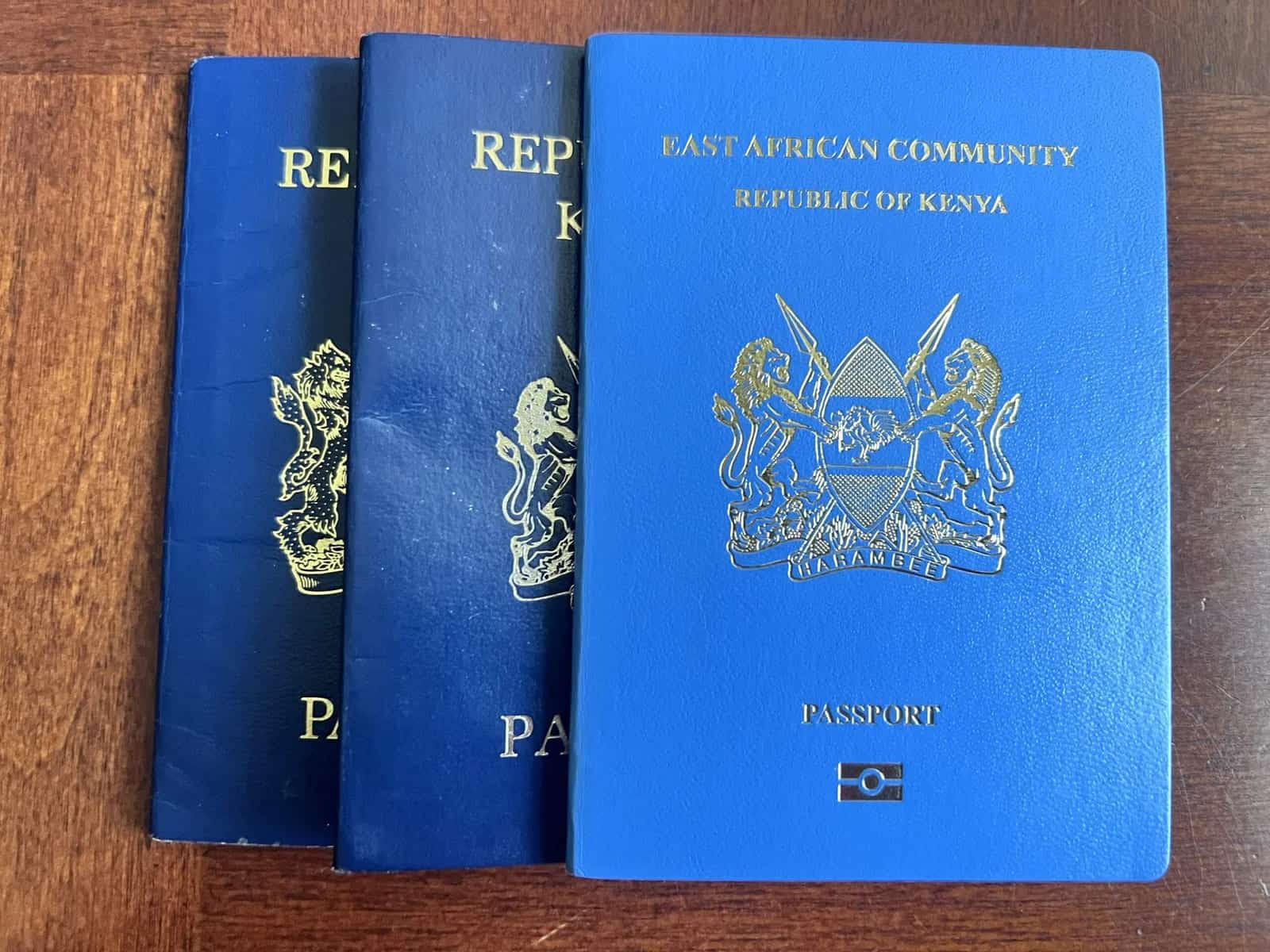 Blue Kenyan passports with the East African Community emblem, stacked on a wooden surface.