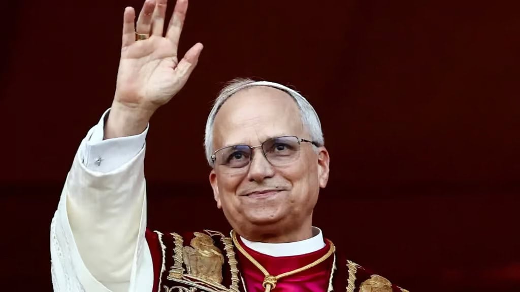 A senior man in religious attire waving with a warm smile.