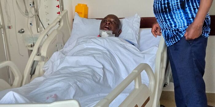 Patient in hospital bed with medical equipment, receiving treatment from healthcare staff.